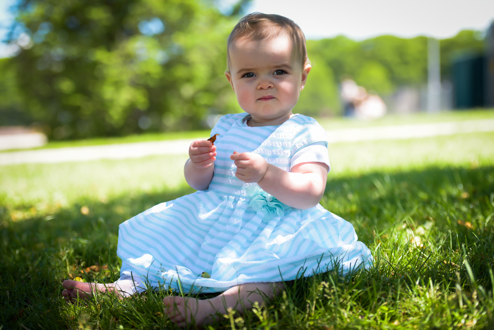 Baby in striped dress sitting on grass
